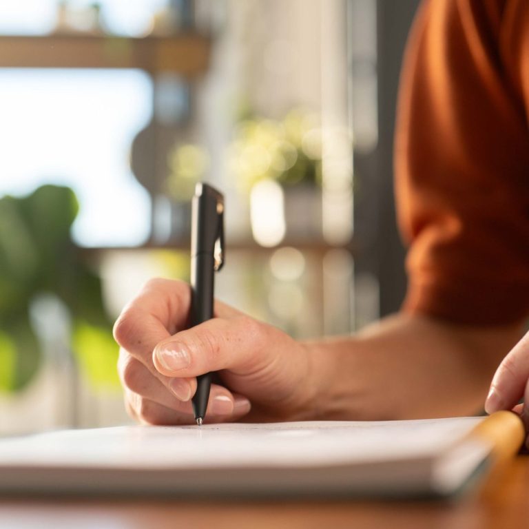 Christina Winter | Marketing für Gründer und Selbstständige Eine Hand schreibt mit einem Stift auf einem Notizblock in einem hellen Raum.